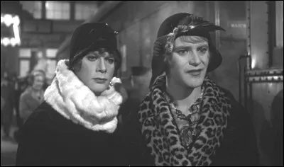 Dans la comédie "Certains l'aiment chaud", que regardent ainsi les deux musiciens travestis en musiciennes ?