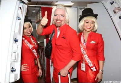 Cette curieuse hôtesse barbue est en fait un grand patron d'industrie, victime (consentante) d'un pari qui l'a fait tenir l'emploi d'hôtesse, en tenue (mini jupe, perruque, maquillage, collants et talons hauts, le temps d'un vol). Qui est  il ?