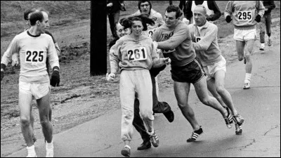 Sur la photo, vous pourrez voir la journaliste Kathrine Switzer en train de courir le marathon de Boston en 1967 ! Elle porte le numéro 261.
Mais, que peut bien faire le type derrière elle et dont on voit difficilement la tête et pourquoi ?