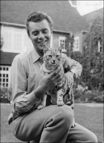Devant sa maison, cet acteur anglais caresse son petit chat tigré (1961).
Indices : acteur né en 1932 - films notables : Les Damnés - Mort à Venise - Portier de nuit