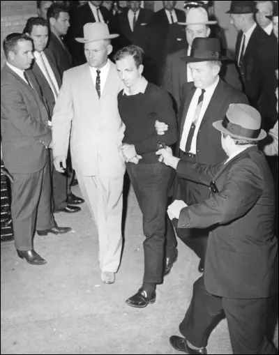 Comment s'appelait le grand gaillard au costume clair auquel L.H.Oswald était menotté peu de temps avant d'être abattu par Jack Ruby ?