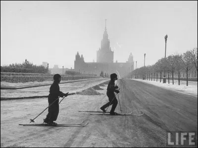1959 : 2 jeunes s'amusent dans la rue. Le commentaire qui accompagne la photo originale explique que les enfants combattent ainsi le froid. Ski parlant, ça irait mieux dans la belle neige blanche comme sur le trottoir. Mais la liberté de pouvoir faire ce qui en temps normal est défendu est plus forte. C'est étonnant de les voir seuls dans cette ville la plus peuplée d'Europe : où est-ce ?