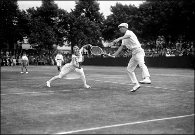 Le 3 juillet 1920, cette photo prise à Roehampton, Londres, illustre une partie de double-mixte au tennis. Il vous faut trouver le joueur (un des 4 mousquetaires) qui partage ce double avec la championne, Suzanne Lenglen (la première dont les robes ne lui allaient qu'aux genoux).
Quel est ce joueur des « 4 mousquetaires » qui firent que l'équipe de France fut victorieuse 6 fois de la Coupe Davis ?