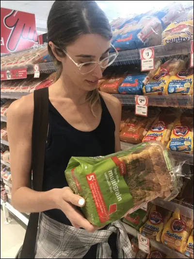 Gastronomie (2) > Cette dame cherche, parmi les ingrédients d'un pain industriel d'origine étrangère, l'un d'eux qui n'y figure pas, à son grand étonnement : lequel ?