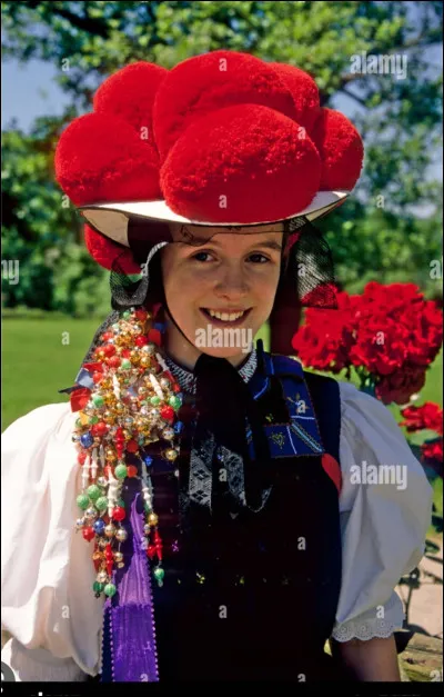 Quelle est la signification des pompons rouges sur le chapeau de cette femme ?