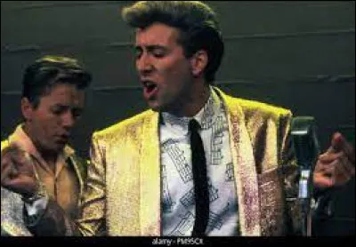 Nicolas Cage joue la confiance avec bananes et veste dorée, en chantant avec son groupe sur scène