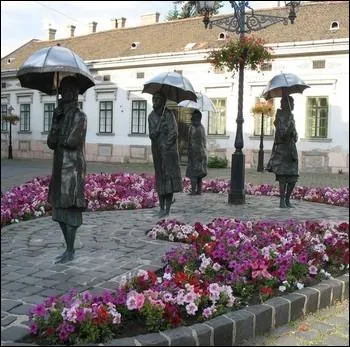 Dans quelle ville peut-on admirer cette composition de statues intitule   Dames aux parapluies  , du sculpteur humaniste hongrois Imre Varga ?