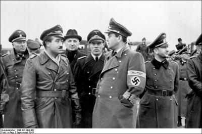 Au premier plan, vous pouvez voir deux personnages allemands. À gauche, le moustachu est un as de l'aviation nazie, surtout pendant la bataille d'Angleterre. À droite, avec un brassard, c'est l'architecte d'Hitler, responsable de l'organisation Todt et ministre de l'Armement. Qui sont-ils ?