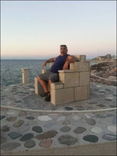 Peut-être le plus grand poète grec du 20e siècle et subissant les foudres des colonels, il connaîtra les camps de rééducation nationale puis la haute surveillance dans différentes îles (Yaros puis Leros et enfin Samos) où chaque soir, il allait contempler le coucher du soleil. Sur la photo, l'auteur de ce quiz dans la chaise élevée pour ce poète à Samos après sa mort. Quel est donc ce grand...